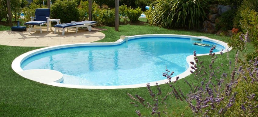 Piscine entourée de gazon synthétique et de végétation dans un jardin privé.