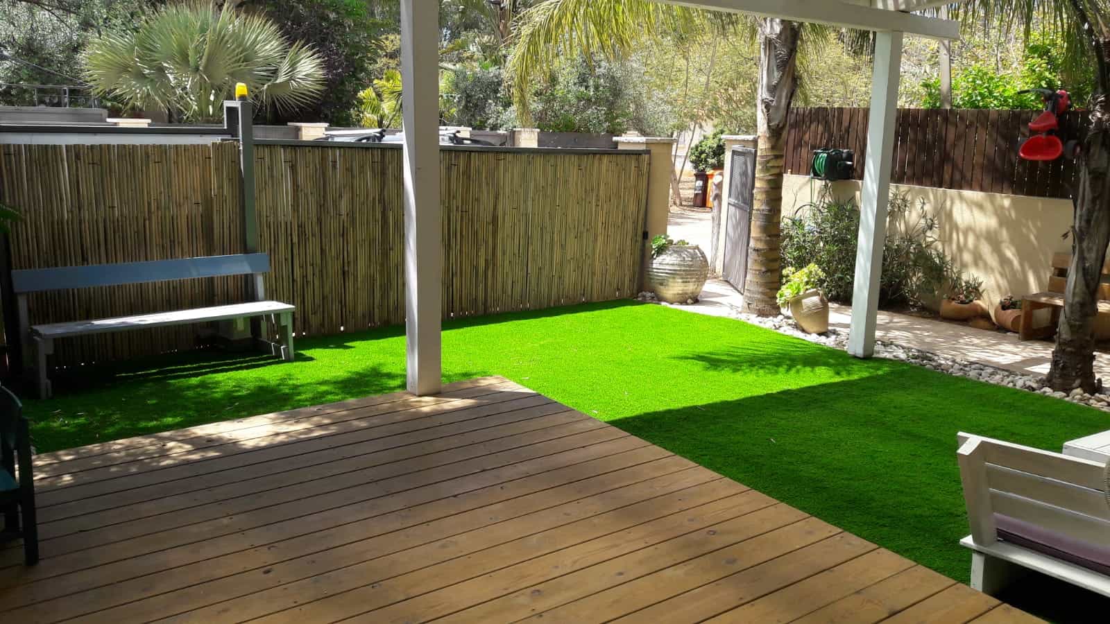 Cour ombragée avec terrasse en bois et gazon synthétique après installation.